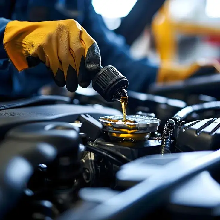 Vidange moteur en cours dans l'atelier : main gantée versant l'huile dans le bloc